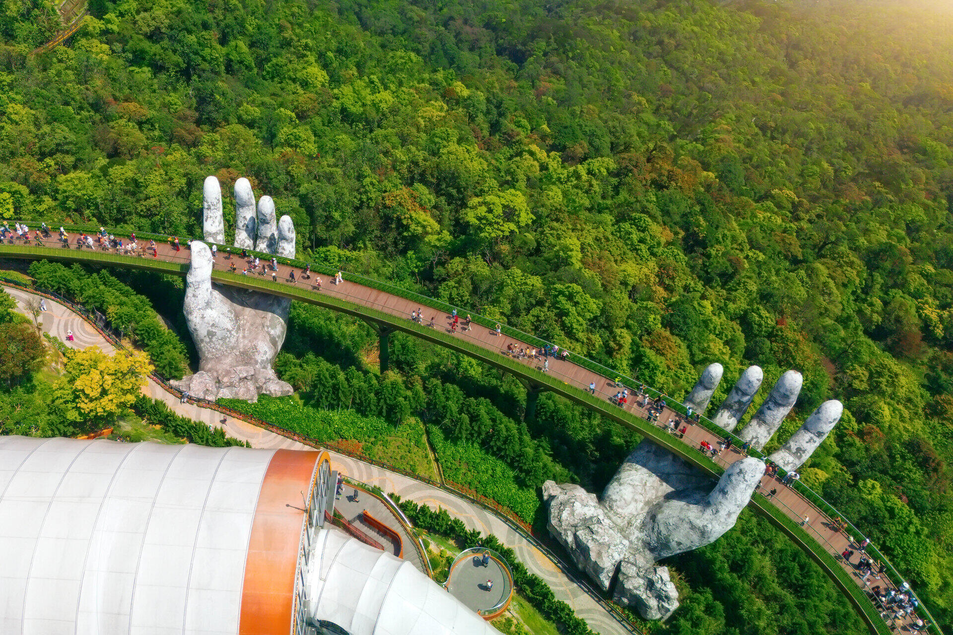 Fu&szlig;g&auml;ngerbr&uuml;cke wird von zwei riesigen steinernen H&auml;nden &uuml;ber dichtem Wald gehalten
