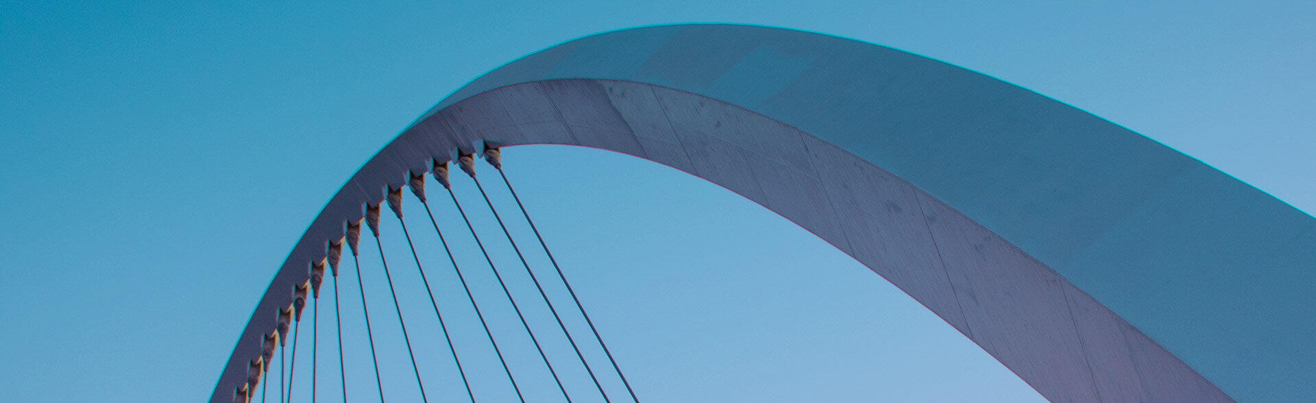 Geschwungener Bogen einer modernen Br&uuml;cke mit gespannten Stahlseilen vor blauem Himmel