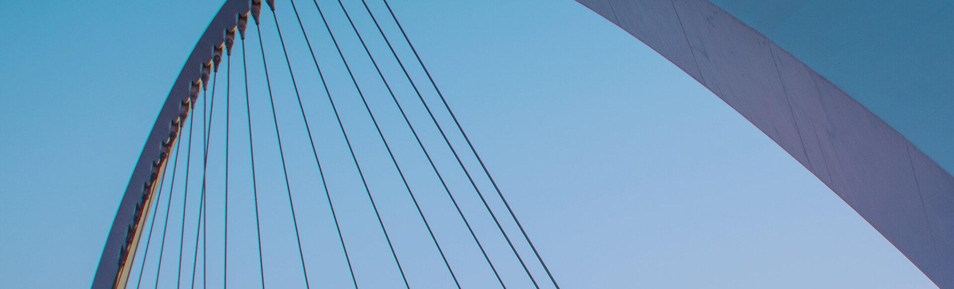 Geschwungener Bogen einer modernen Br&uuml;cke mit Stahlseilen vor blauem Himmel