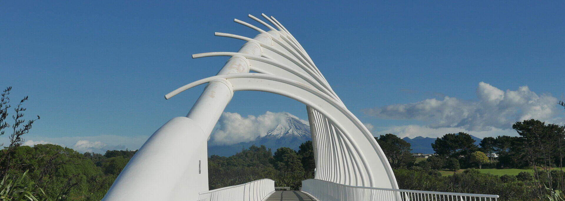 Wei&szlig;e geschwungene Fu&szlig;g&auml;ngerbr&uuml;cke Te Rewa Rewa vor blauem Himmel und Bergkulisse