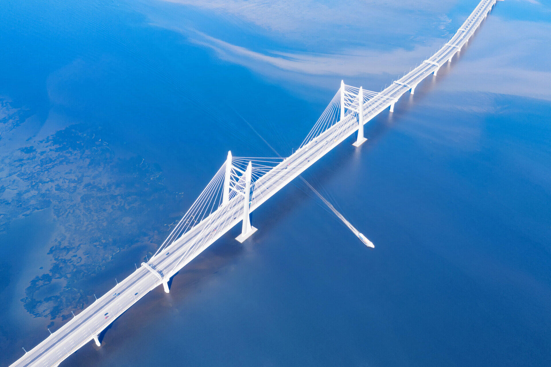 Luftaufnahme einer wei&szlig;en Schr&auml;gseilbr&uuml;cke &uuml;ber blauem Wasser mit einem Boot