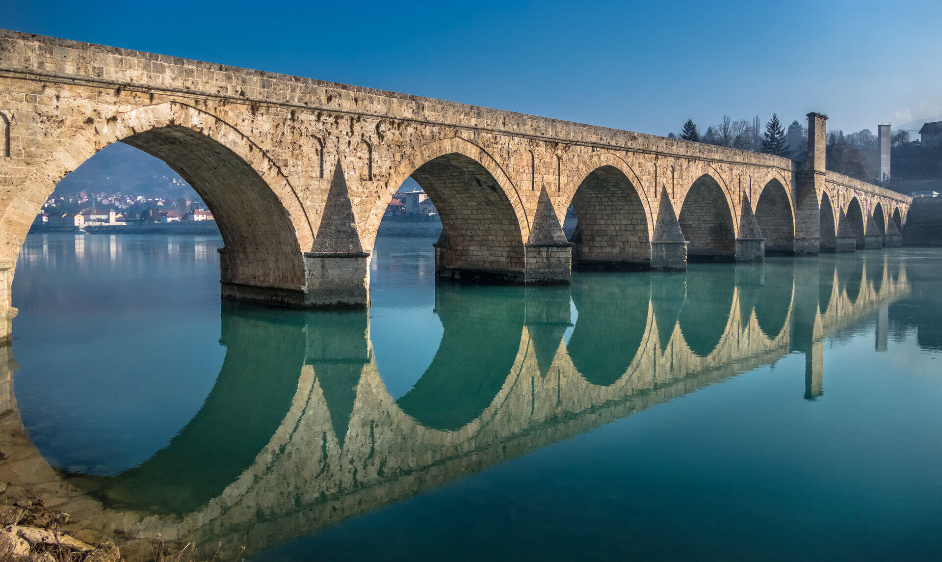 Steinerne Bogenbr&uuml;cke mit mehreren Rundb&ouml;gen spiegelt sich im ruhigen Flusswasser