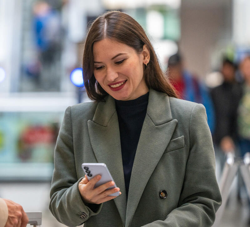 Karina Malancea zeigt einem Reisenden mit Rollkoffer l&auml;chelnd etwas auf ihrem Smartphone im Bahnhof