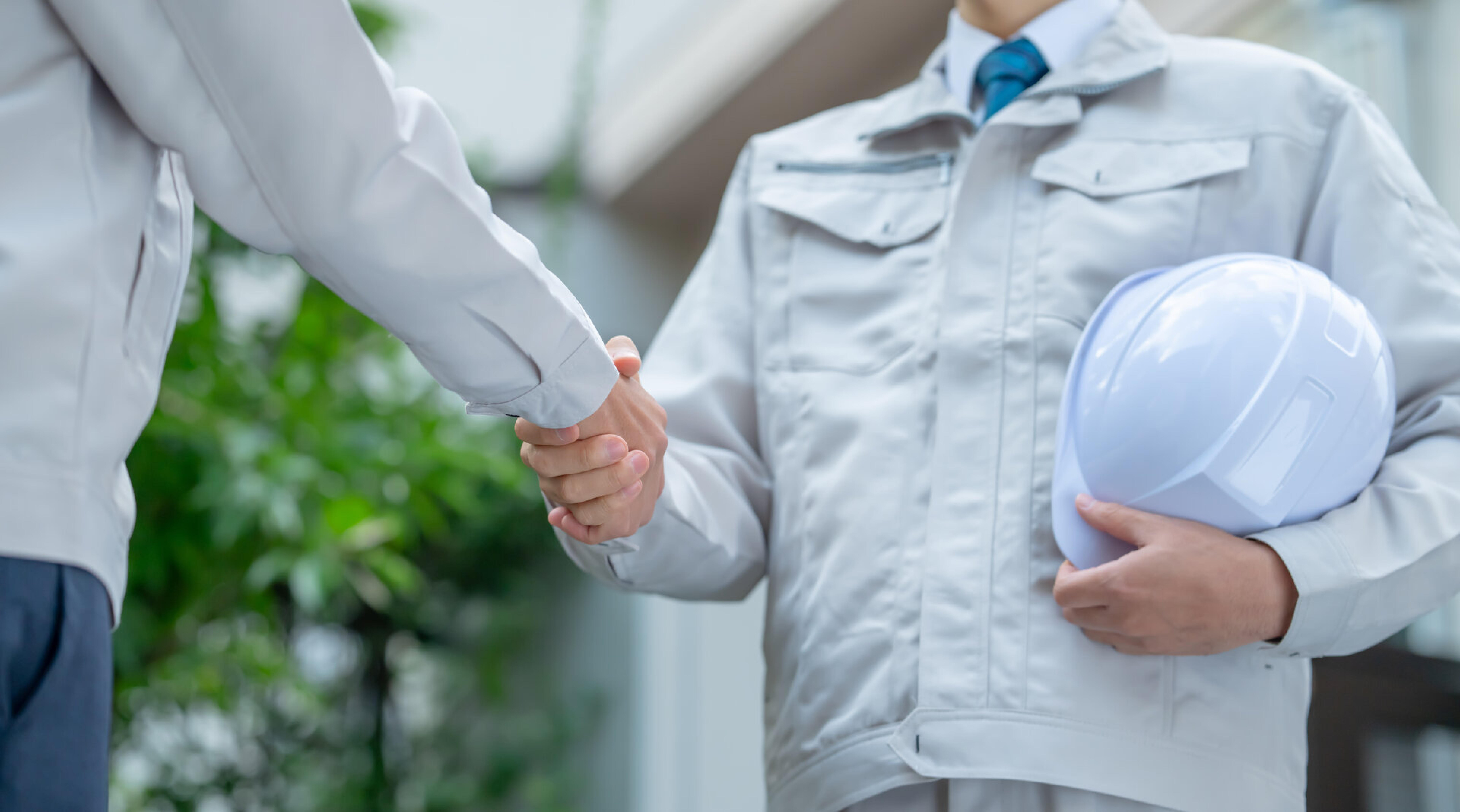 Handschlag zweier Personen in Arbeitskleidung, eine h&auml;lt einen Schutzhelm