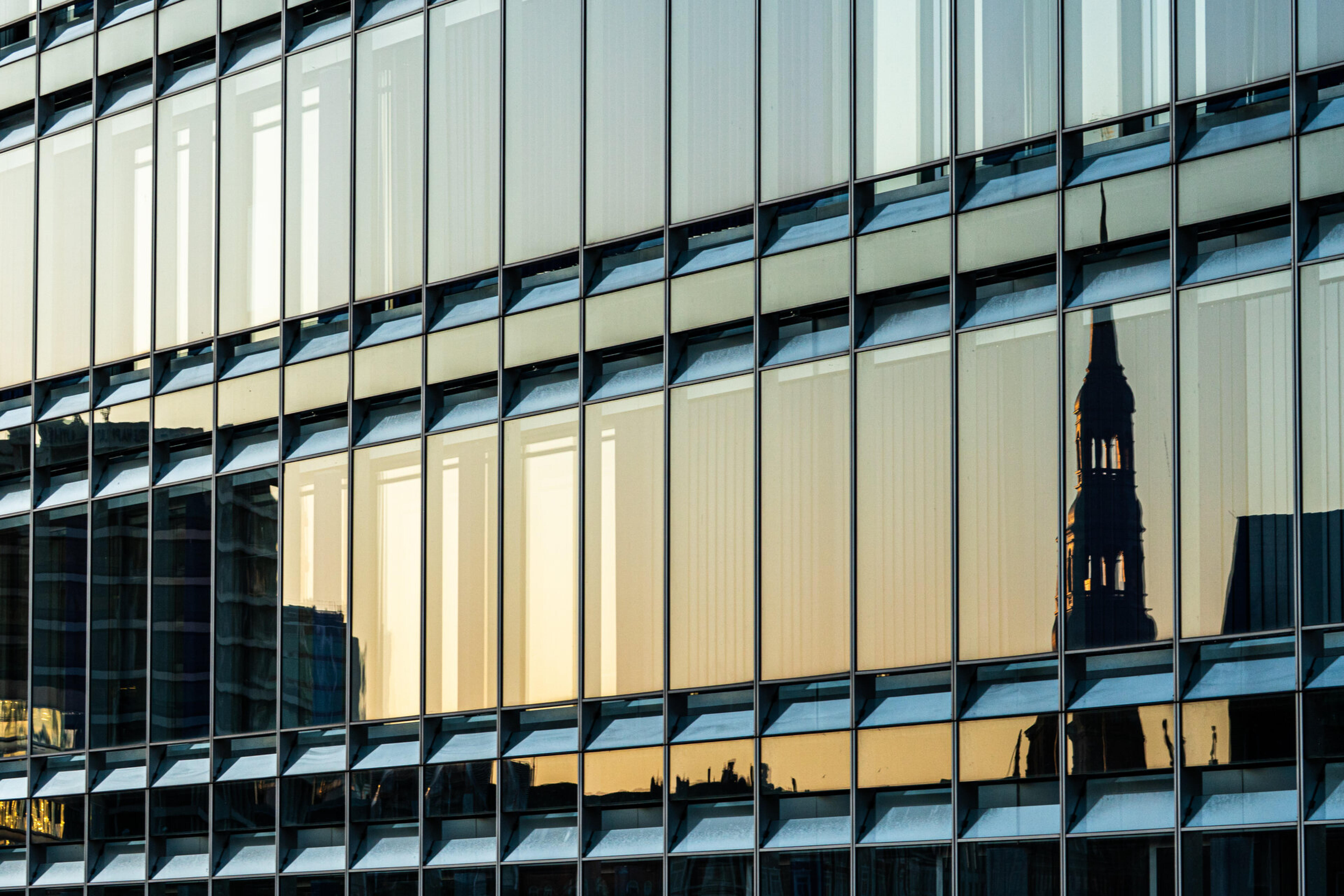 Glasfassade eines B&uuml;rogeb&auml;udes spiegelt einen Kirchturm bei Sonnenuntergang