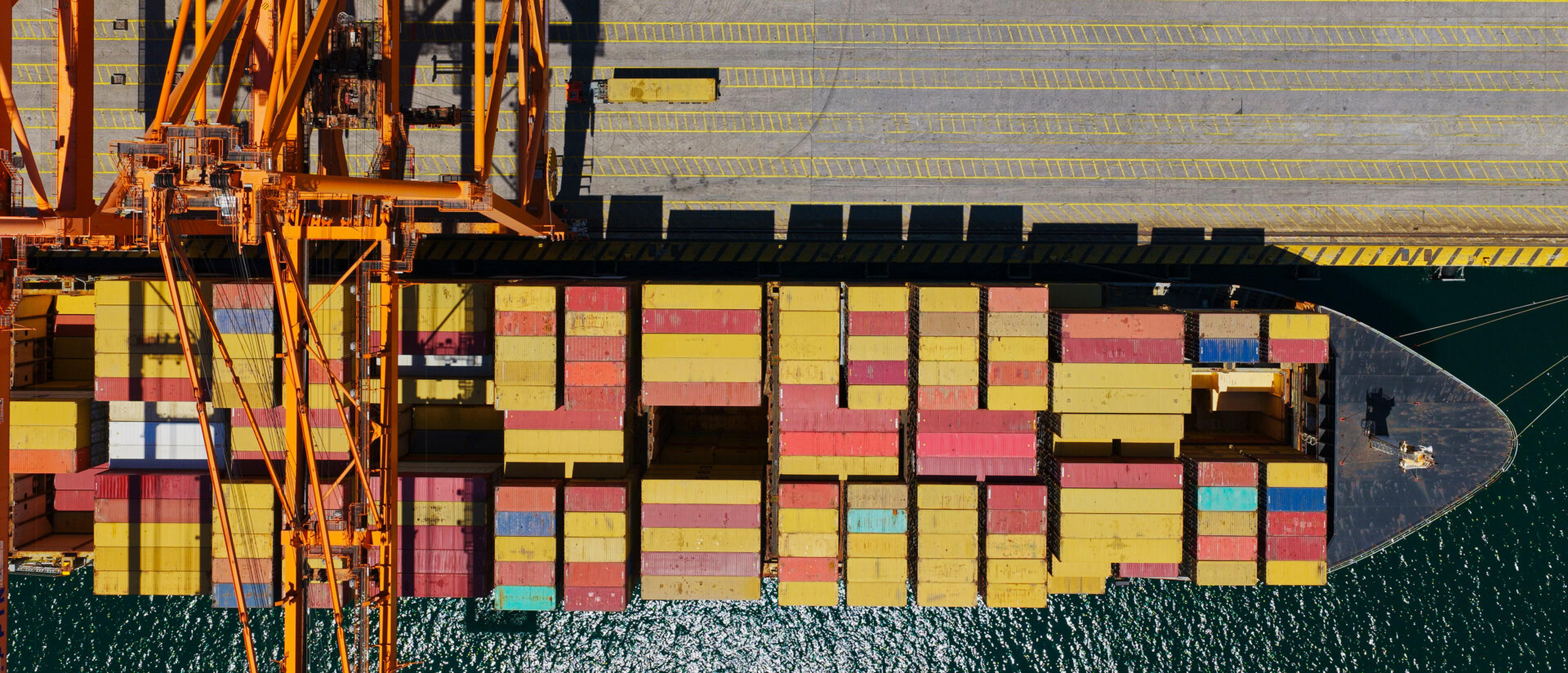 Luftaufnahme eines Containerschiffs mit bunten Containern und Verladekran am Hafenkai