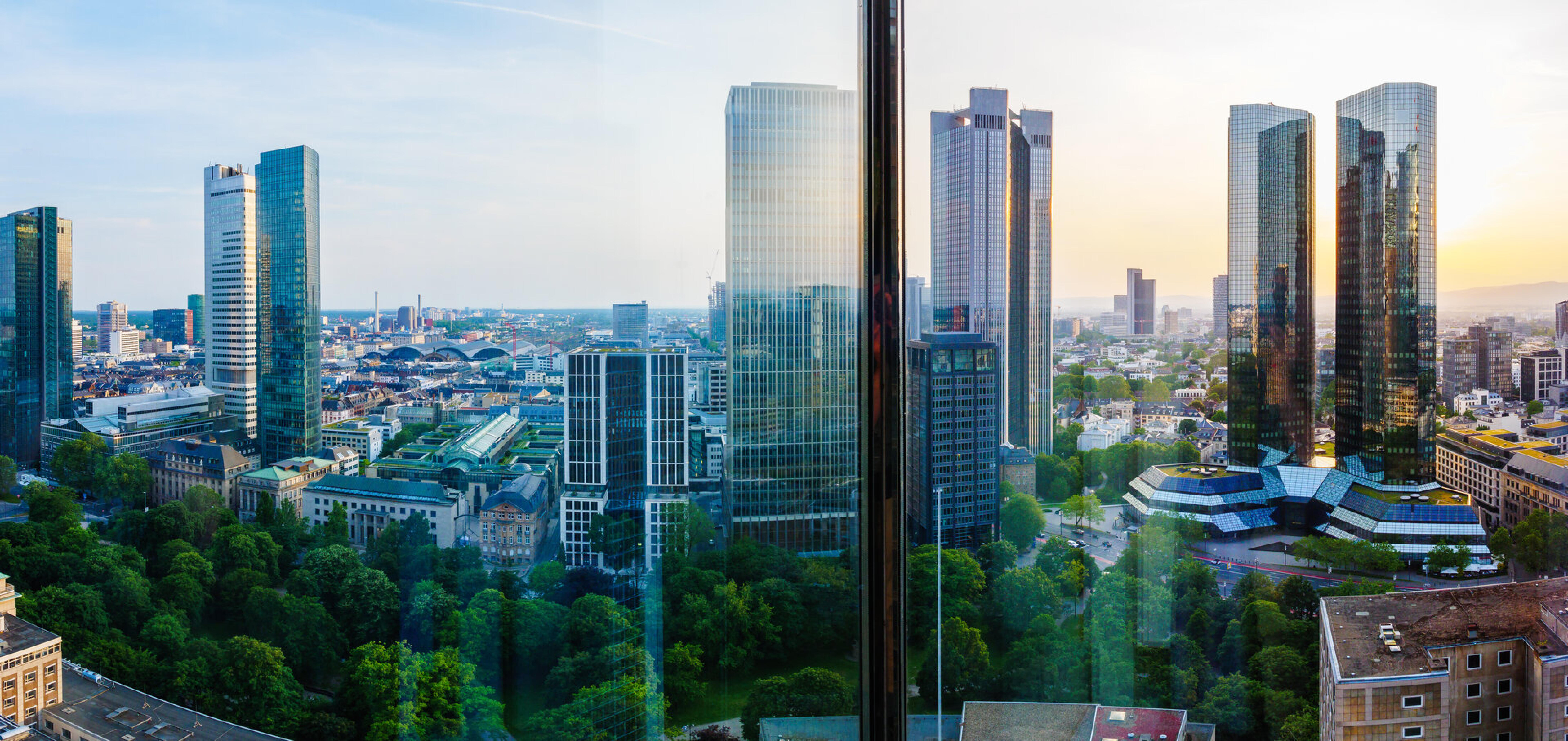 Blick &uuml;ber die Frankfurter Skyline mit Bankenhochh&auml;usern und Gr&uuml;nanlagen im Abendlicht