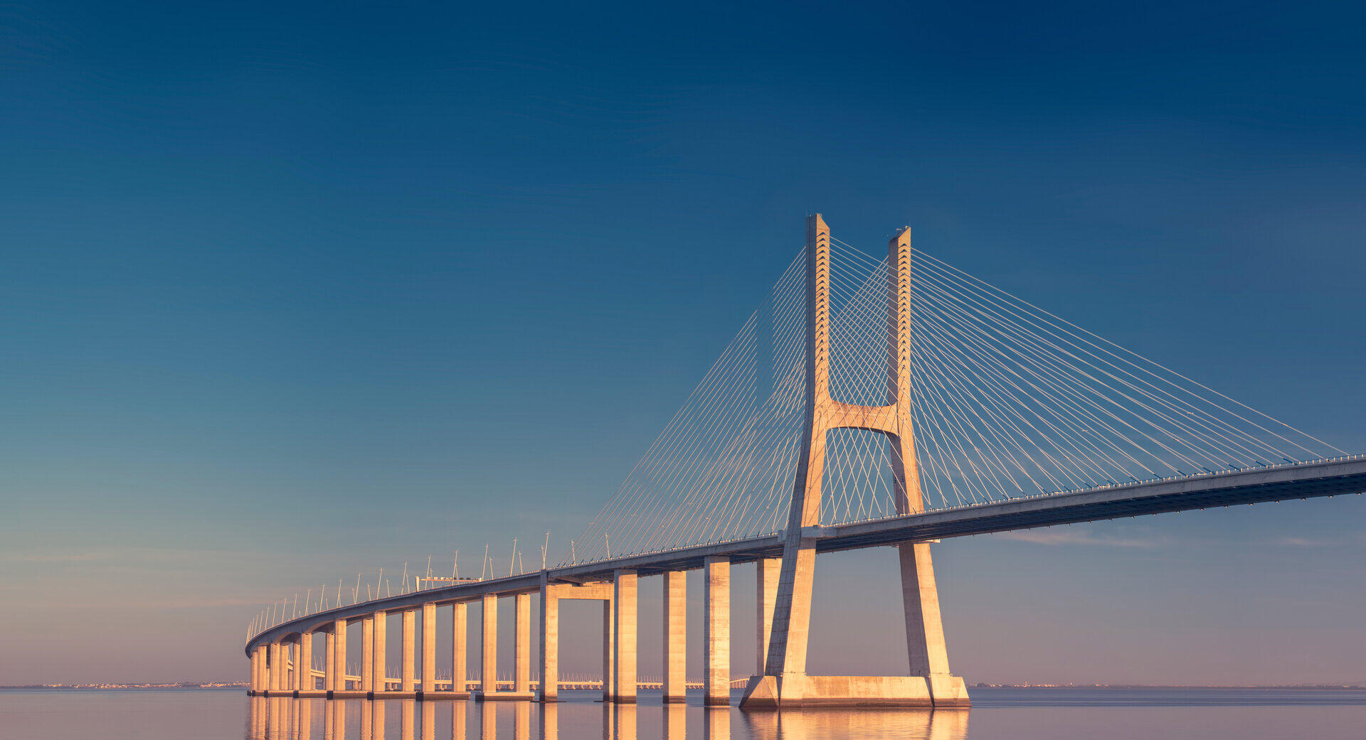Schr&auml;gseilbr&uuml;cke im warmen Abendlicht &uuml;ber ruhigem Wasser