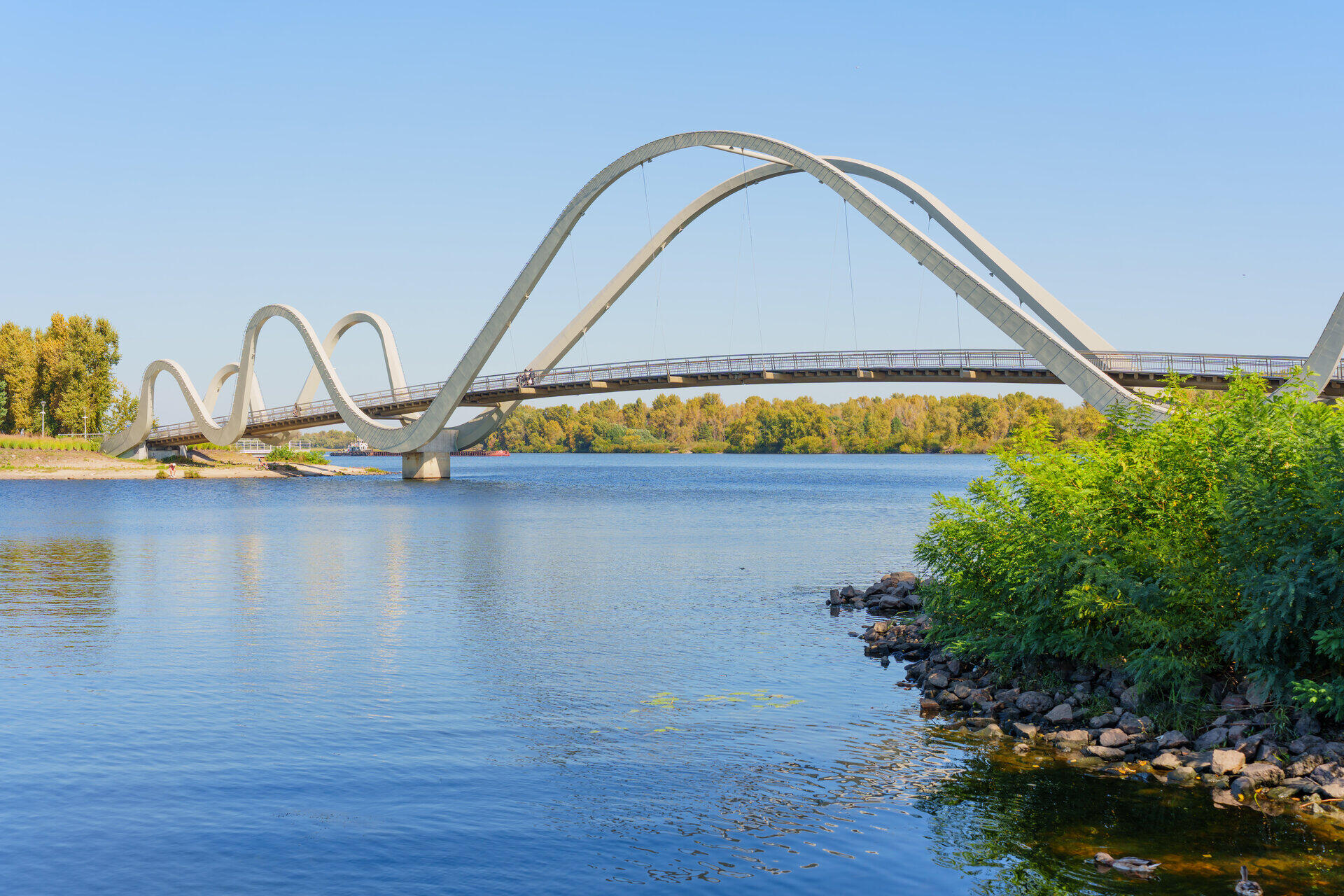 Geschwungene Fu&szlig;g&auml;ngerbr&uuml;cke mit mehreren B&ouml;gen &uuml;ber einem breiten Fluss