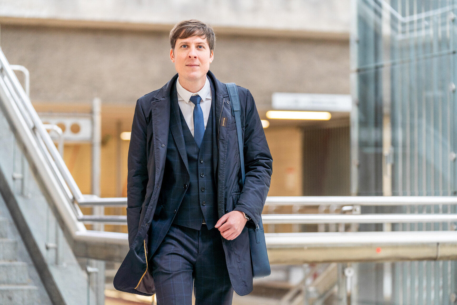 Dmitry Novitsky im Anzug mit Umh&auml;ngetasche geht eine Treppe zwischen Gel&auml;ndern hinab