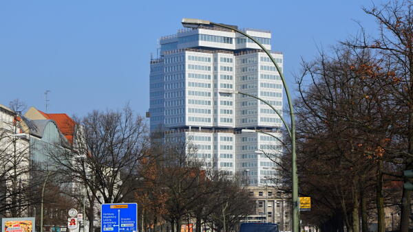 B&uuml;rohochhaus mit Glasfassade hinter kahlen B&auml;umen vor blauem Himmel
