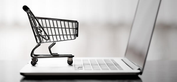 Miniatur-Einkaufswagen steht auf der Tastatur eines aufgeklappten Laptops