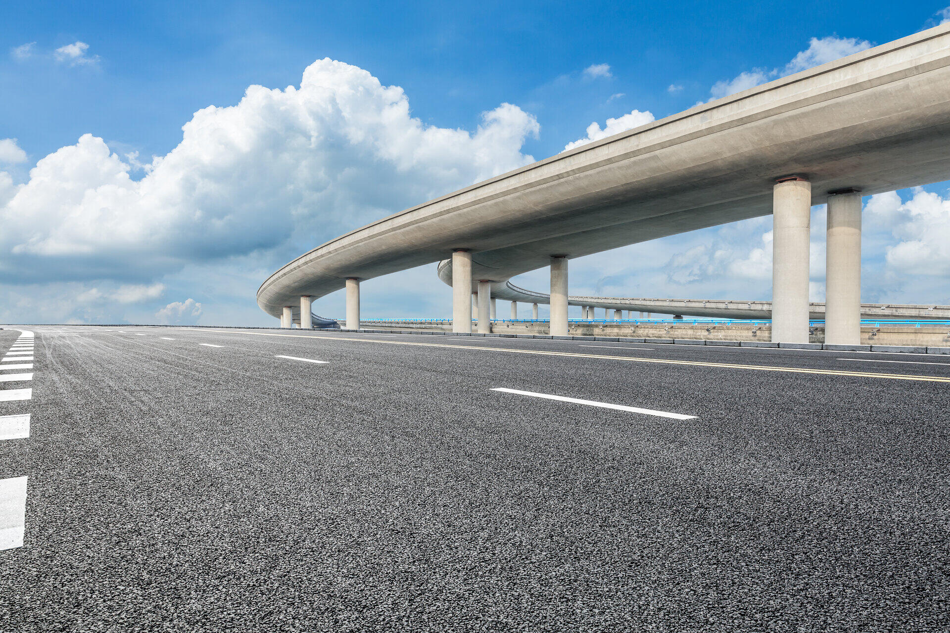 Geschwungene Hochstra&szlig;e auf Betonpfeilern neben einer leeren Fahrbahn unter Wolken