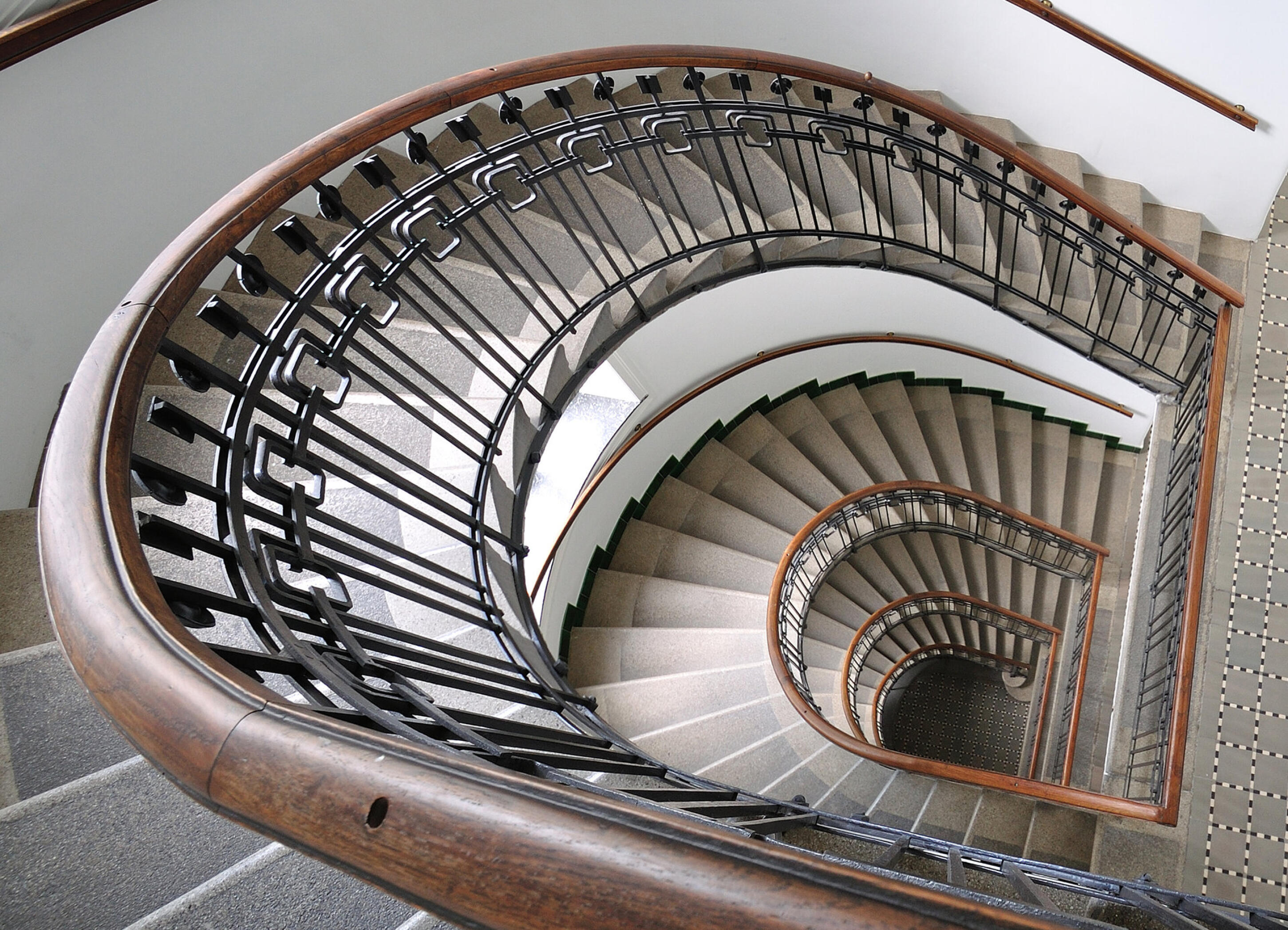 Blick von oben in ein spiralf&ouml;rmiges Treppenhaus mit Holzhandlauf und schmiedeeisernem Gel&auml;nder