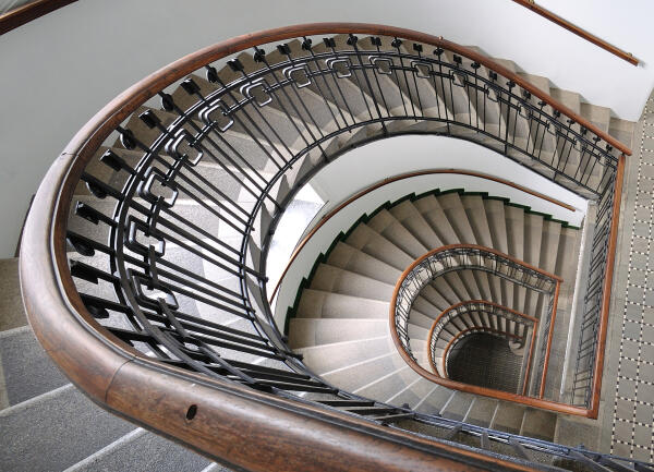 Blick von oben in ein spiralf&ouml;rmiges Treppenhaus mit Holzhandlauf und schmiedeeisernem Gel&auml;nder
