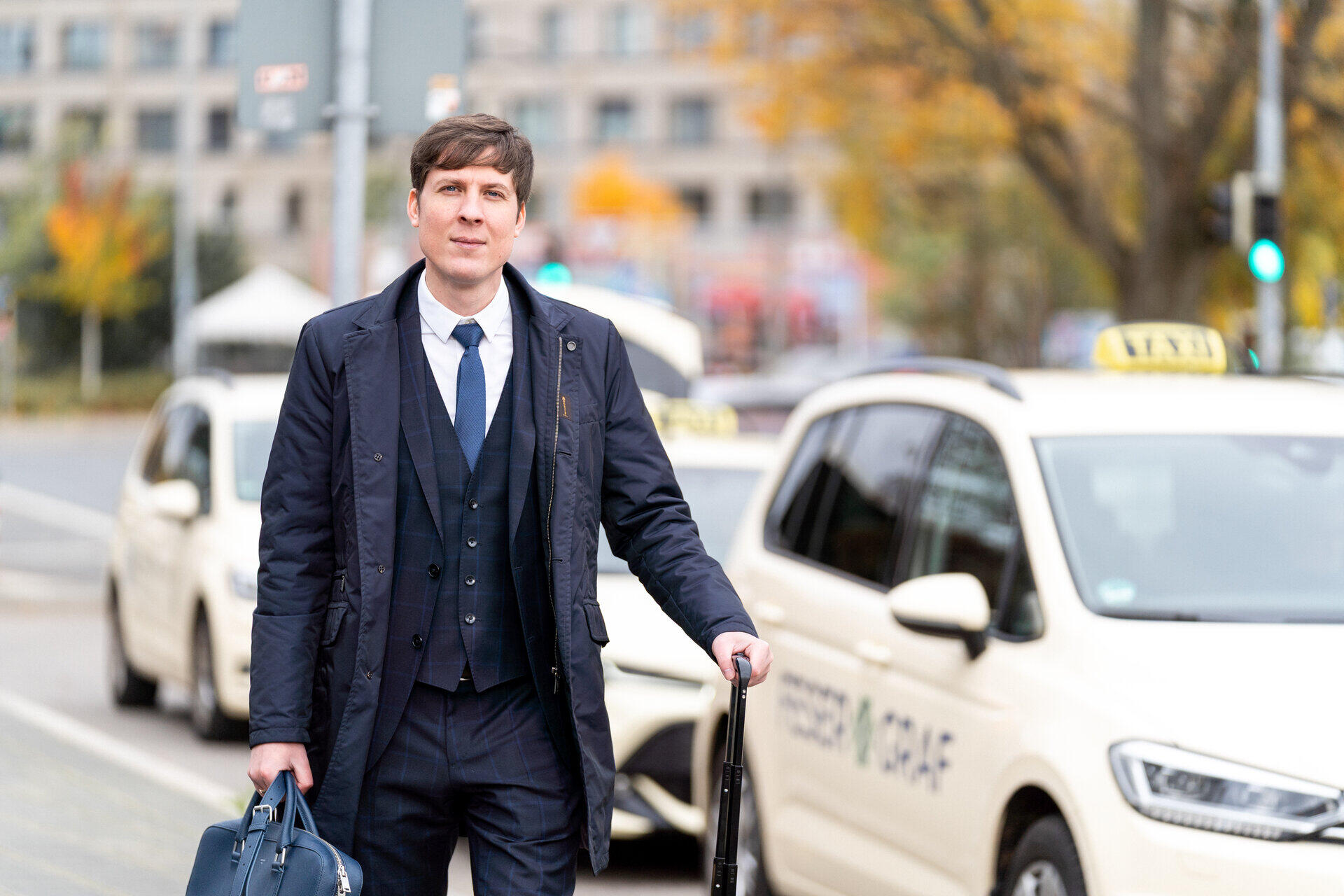 Dmitry Novitsky mit Tasche und Rollkoffer an einer Stra&szlig;e mit Taxis