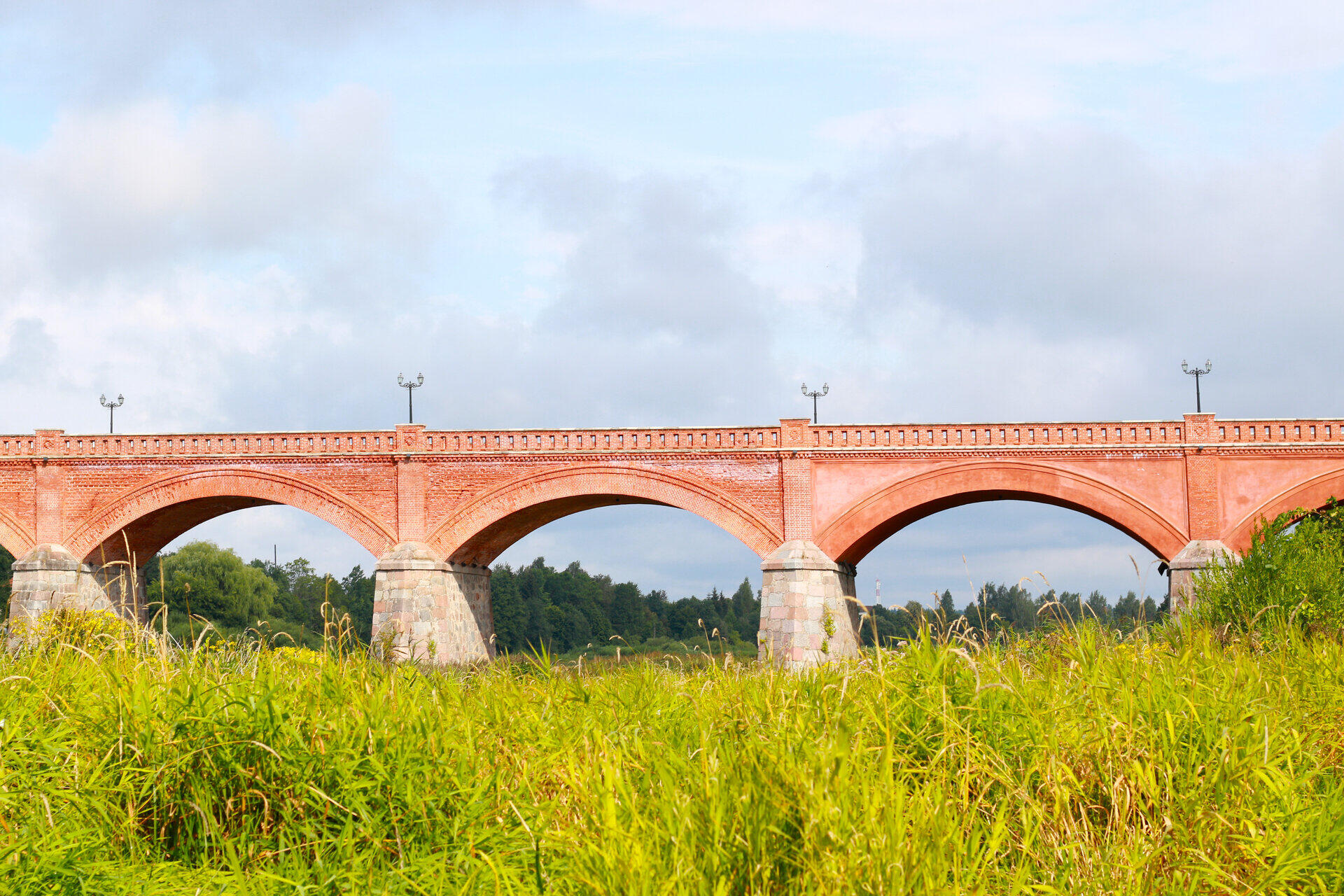 Alte Backsteinbr&uuml;cke mit mehreren B&ouml;gen und Laternen hinter einer gr&uuml;nen Wiese