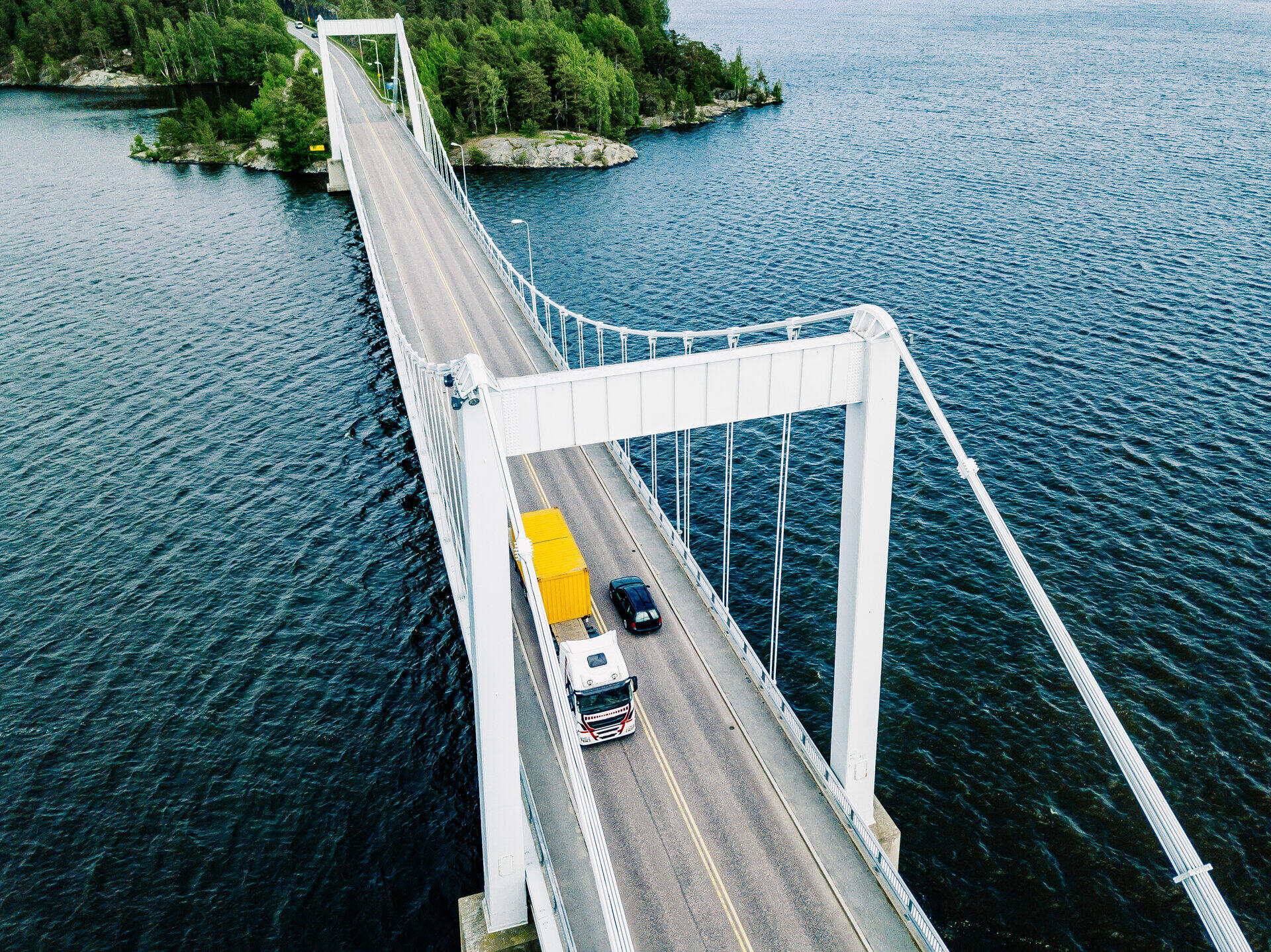 H&auml;ngebr&uuml;cke &uuml;ber dunkles Wasser, ein Lkw mit gelbem Auflieger &uuml;berquert die Fahrbahn