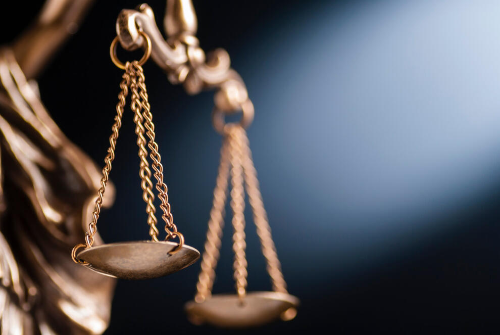 Nahaufnahme der Waagschalen einer Justitia-Figur aus Messing vor dunklem Hintergrund
