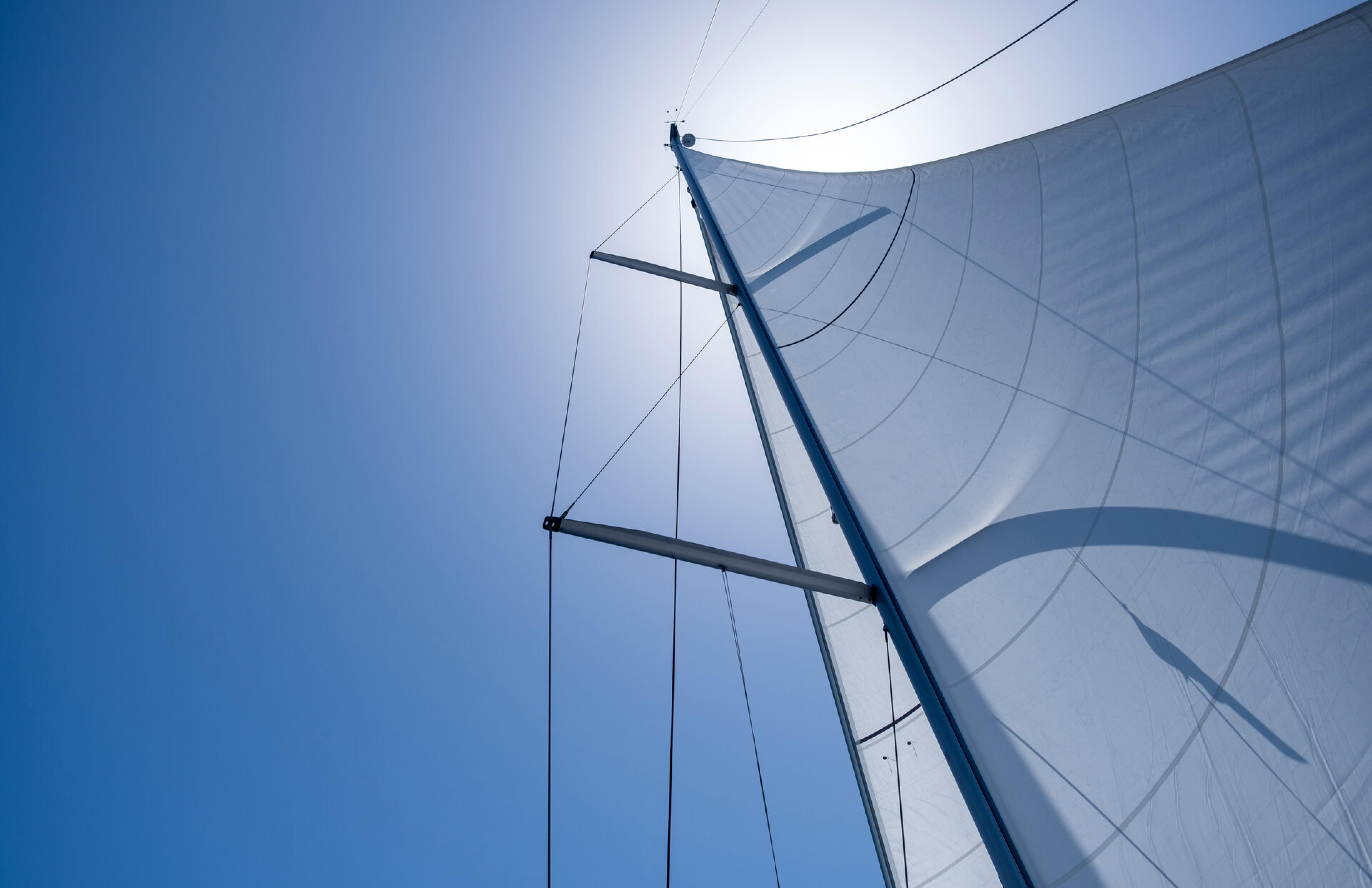 Mast und wei&szlig;es Segel einer Segelyacht von unten vor strahlend blauem Himmel