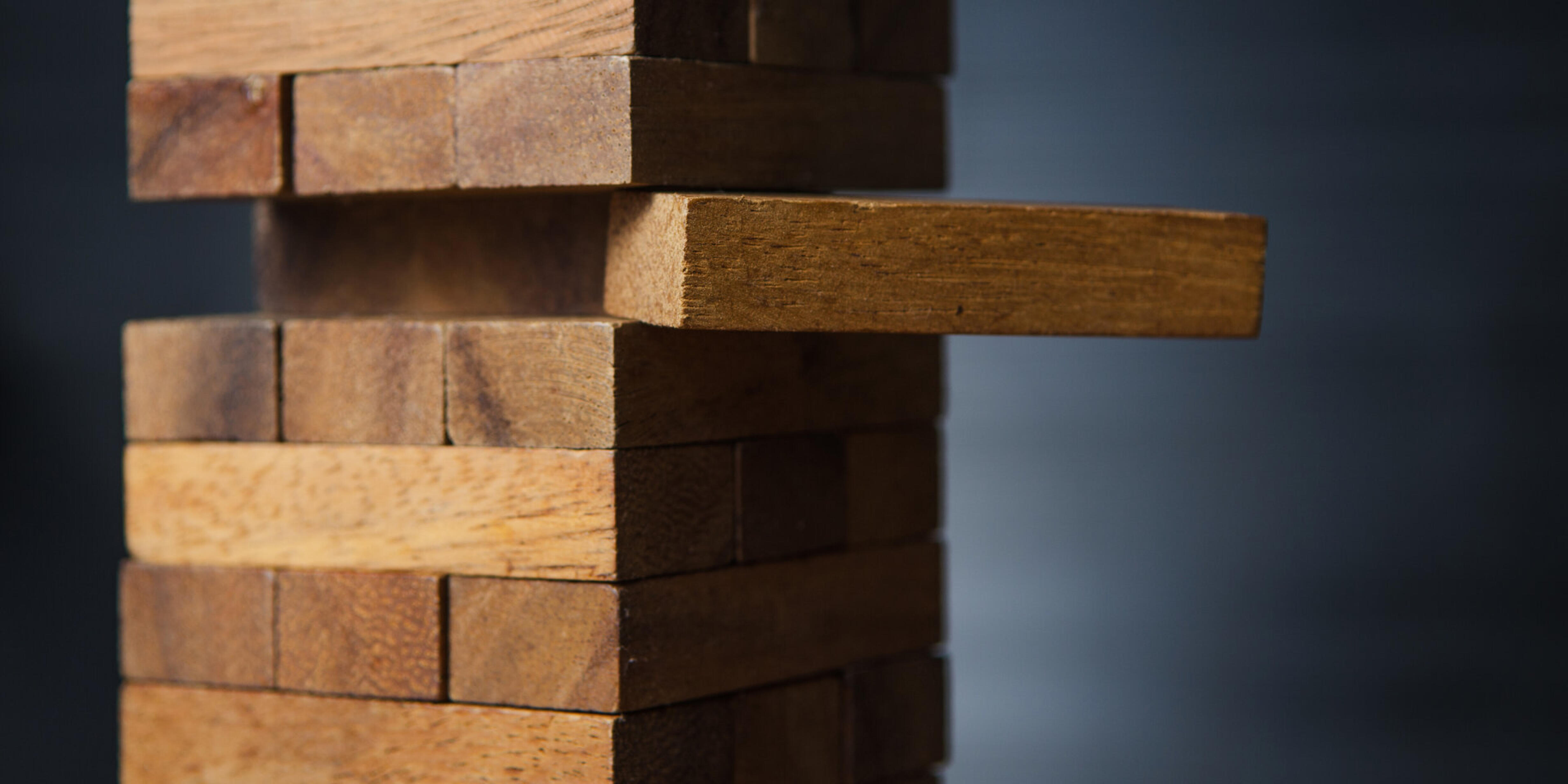 Ein Holzkl&ouml;tzchen wird seitlich aus einem Jenga-Turm herausgezogen