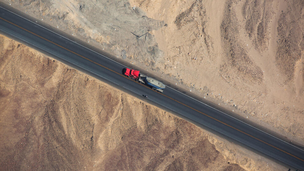 Luftaufnahme eines roten Lkw mit Auflieger auf einer Landstra&szlig;e durch W&uuml;stenlandschaft