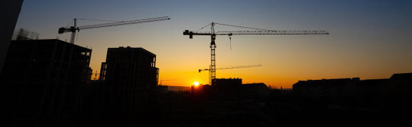 Silhouetten von Baukr&auml;nen und Hochh&auml;usern vor einem orangefarbenen Sonnenuntergang