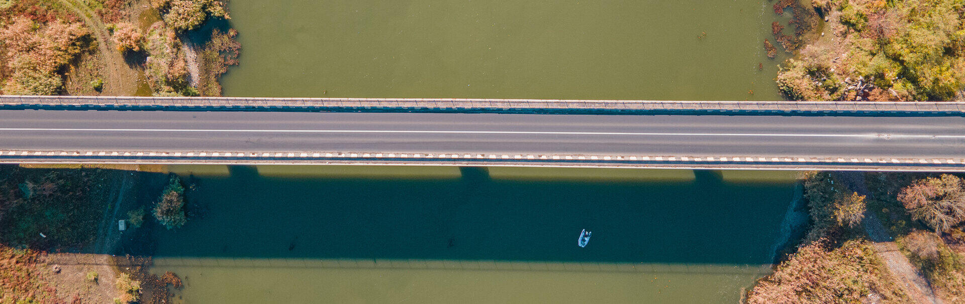 Luftaufnahme einer Stra&szlig;enbr&uuml;cke &uuml;ber einen gr&uuml;nen Fluss mit herbstlichen Ufern