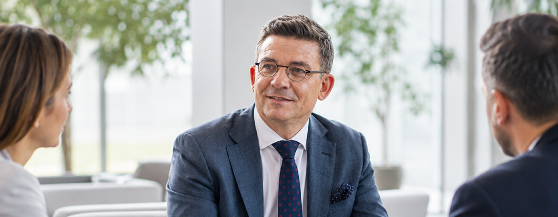 Anwalt im Anzug erkl&auml;rt zwei Gespr&auml;chspartnern Unterlagen bei einer Besprechung im hellen Foyer