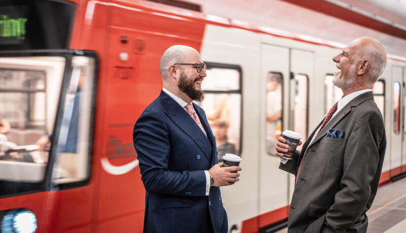 Zwei Maxfeld-Anw&auml;lte im Gespr&auml;ch mit Kaffeebechern vor einer roten U-Bahn