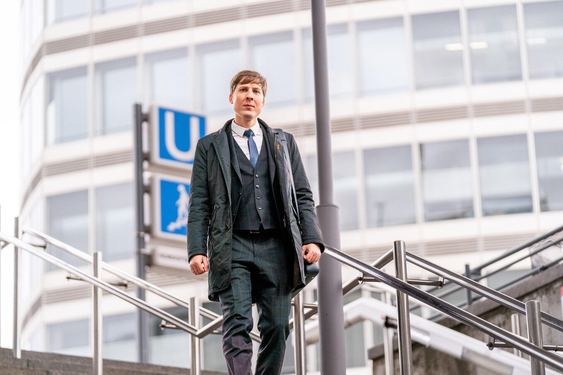Dmitry Novitsky im Mantel steigt eine Treppe am U-Bahn-Aufgang vor einem Hochhaus hinauf