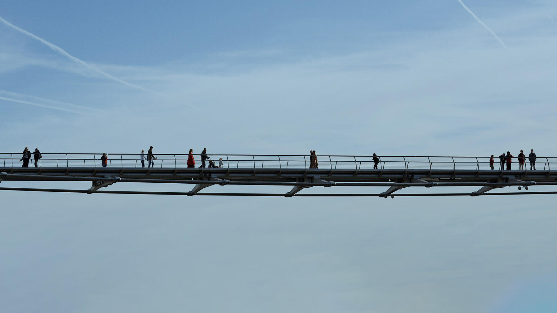 Fu&szlig;g&auml;nger als Silhouetten auf einer schlanken Br&uuml;cke vor blauem Himmel