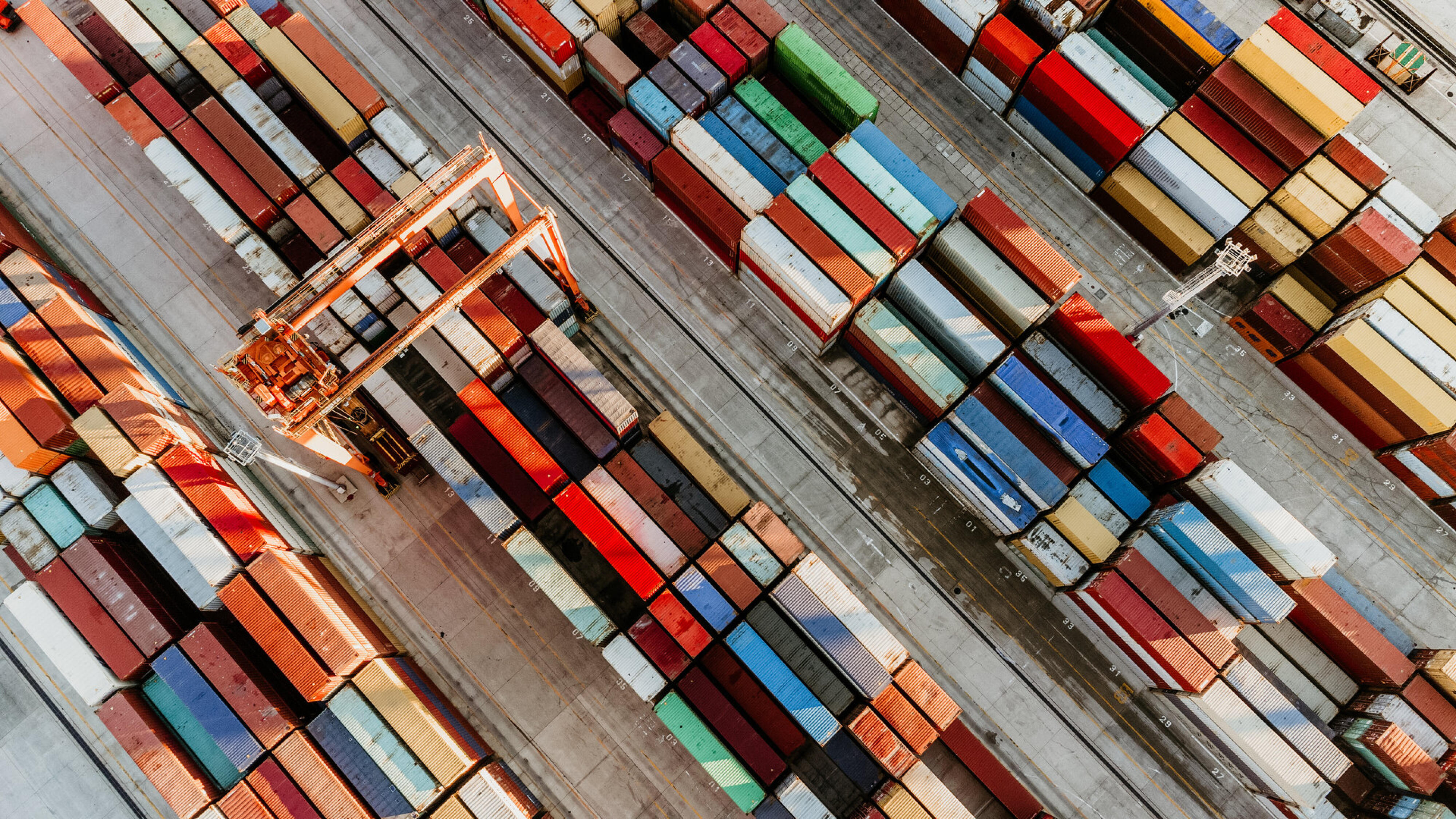 Containerterminal von oben mit Kran zwischen Reihen aus Frachtcontainern