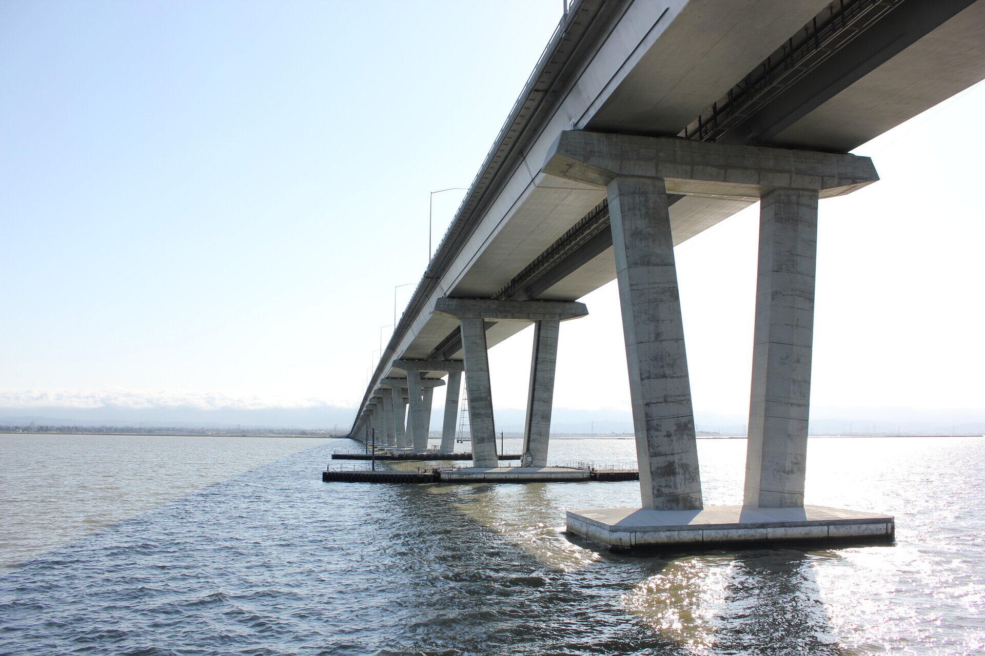 Blick von unten auf massive Betonpfeiler einer Br&uuml;cke &uuml;ber Wasser