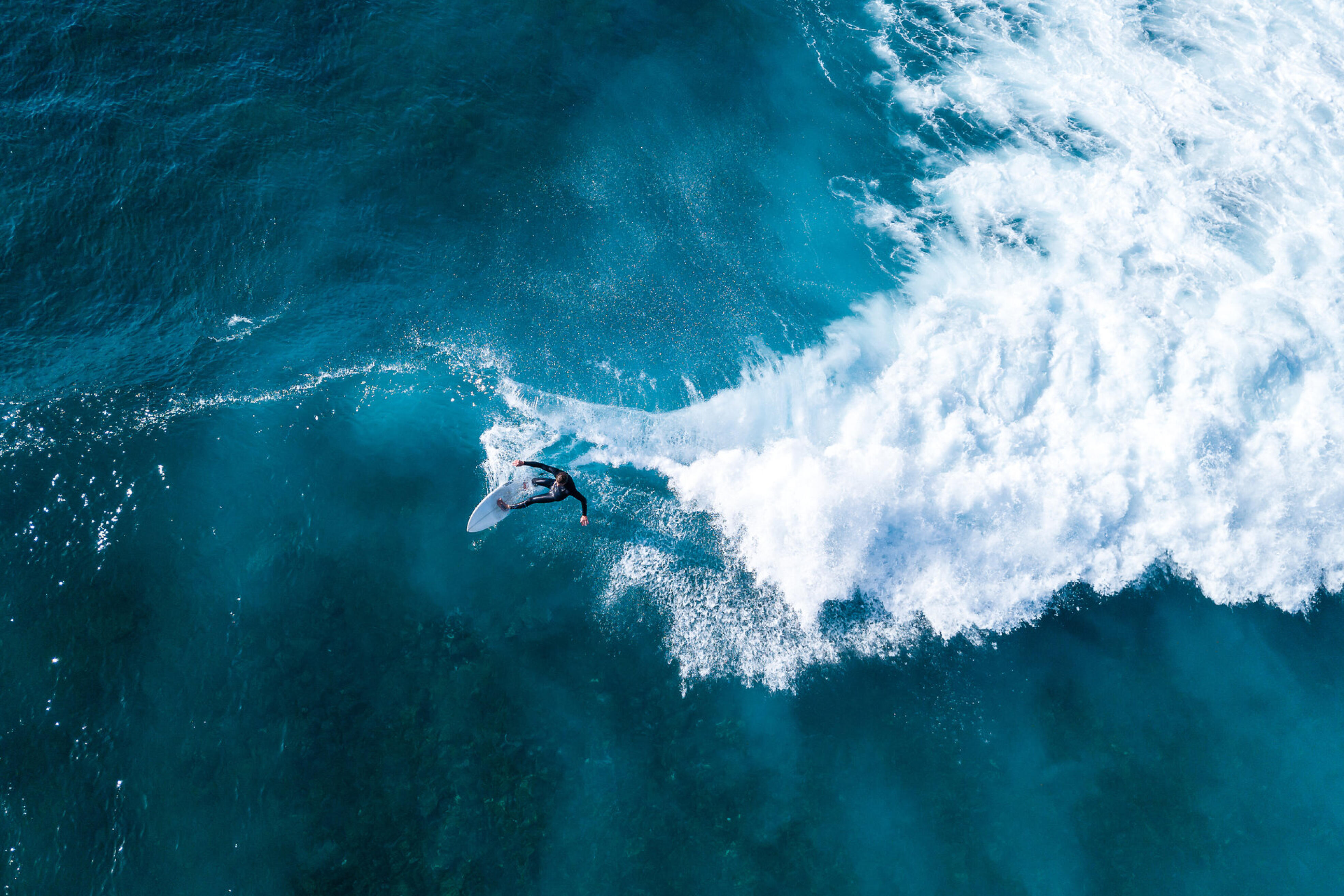 Surfer von oben beim Reiten einer sch&auml;umenden Welle im offenen Meer