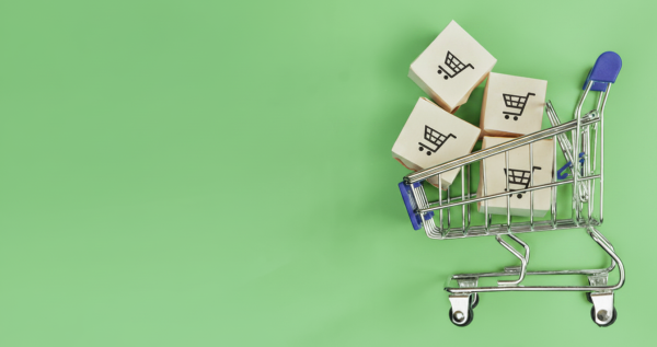 Miniatur-Einkaufswagen mit Paketen auf gr&uuml;nem Hintergrund