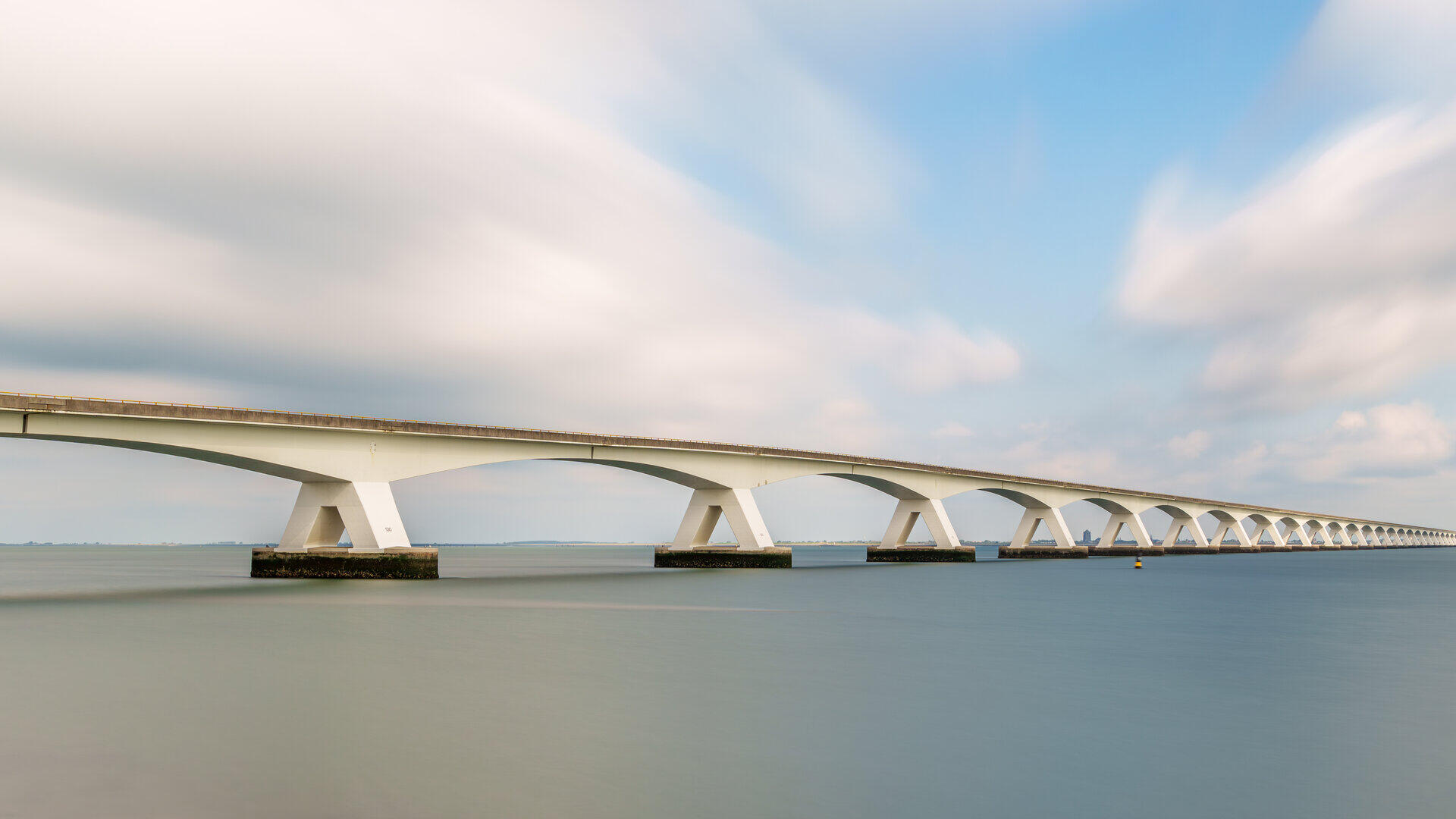Lange flache Br&uuml;cke mit zahlreichen Pfeilern &uuml;ber ruhigem Wasser