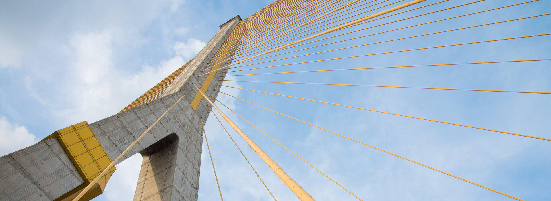 Pylon einer Schr&auml;gseilbr&uuml;cke mit gelben Tragseilen vor blauem Himmel, Froschperspektive
