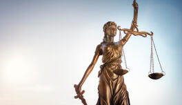 Bronzestatue der Justitia mit Waage und Schwert vor hellem Himmel
