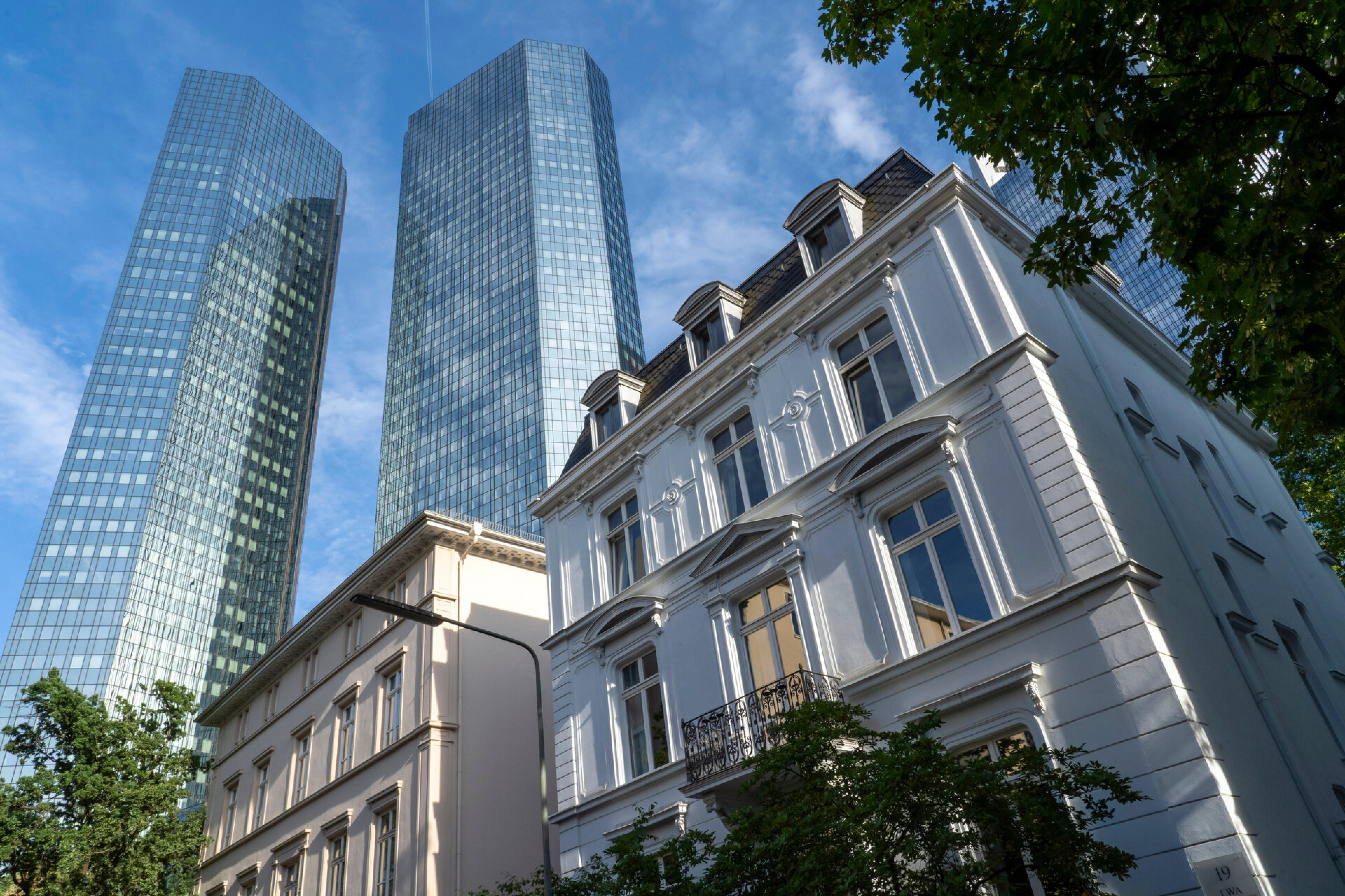 Historisches Altbaugeb&auml;ude vor zwei modernen Glashochh&auml;usern unter blauem Himmel