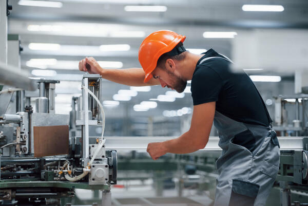 Arbeiter mit orangefarbenem Schutzhelm bedient eine Verpackungsmaschine in einer Produktionshalle
