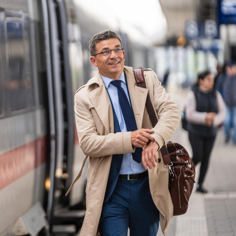 Rechtsanwalt Daniel G&ouml;&szlig;ling im Trenchcoat auf dem Bahnsteig neben einem ICE