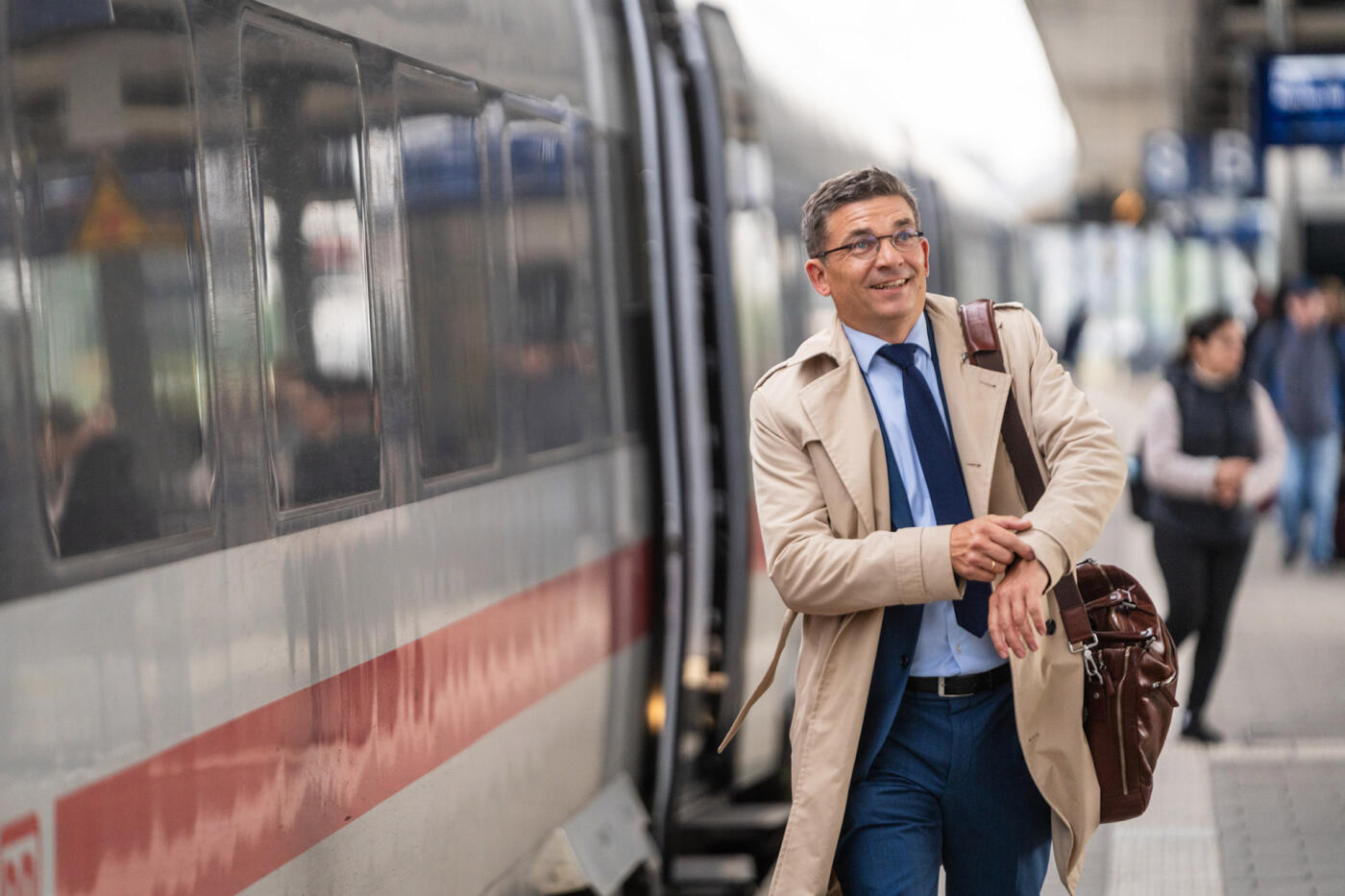Rechtsanwalt Daniel G&ouml;&szlig;ling mit Trenchcoat und Aktentasche auf einem Bahnsteig
