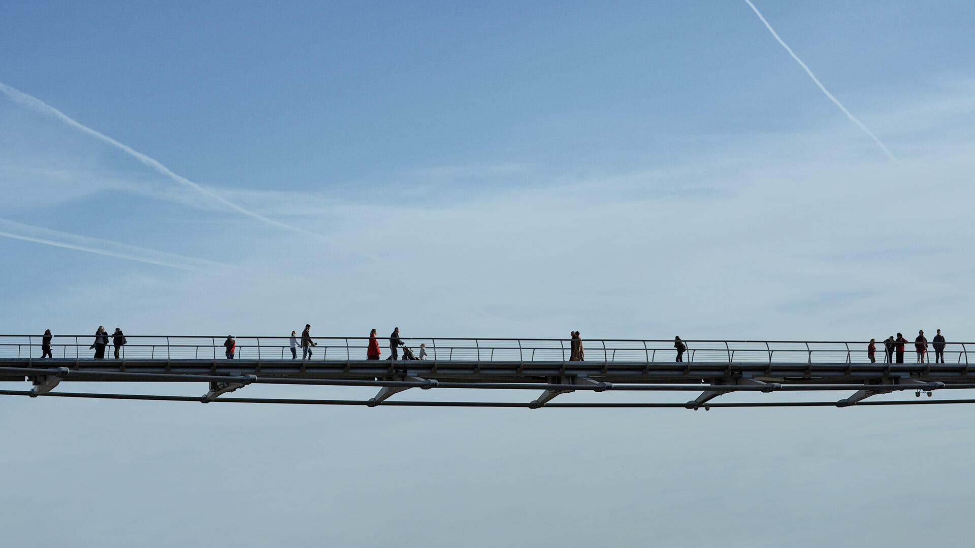 Fu&szlig;g&auml;nger als Silhouetten auf einer schlanken Br&uuml;cke vor blauem Himmel