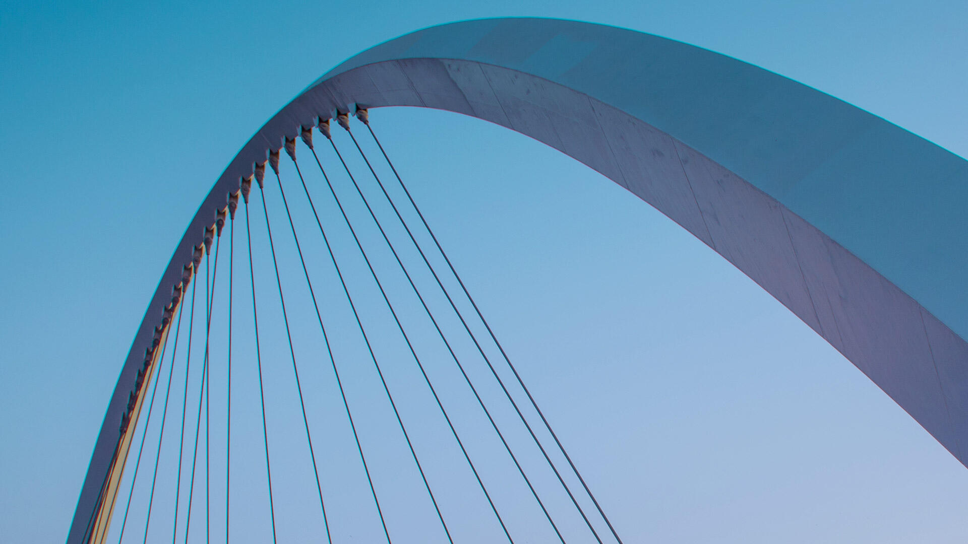 Geschwungener Bogen einer modernen Br&uuml;cke mit Stahlseilen vor blauem Himmel